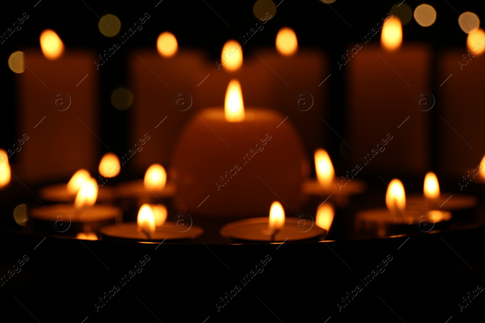 Photo of Many burning candles on dark surface, closeup