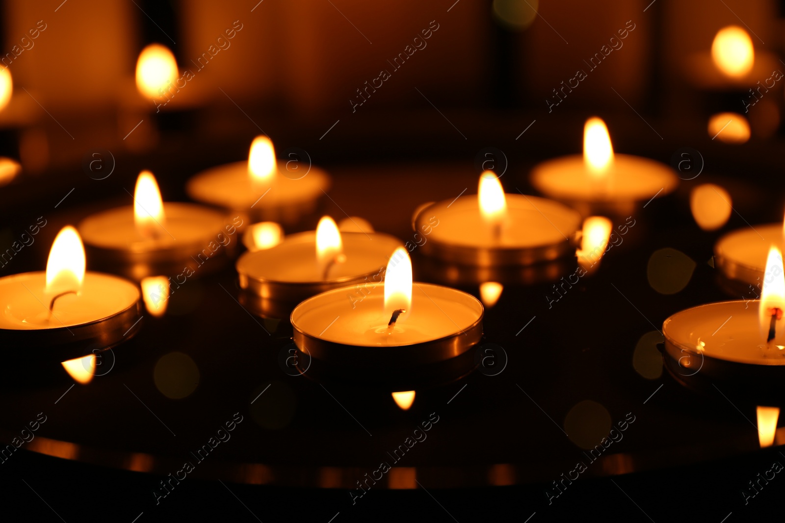 Photo of Many burning candles on dark surface, closeup