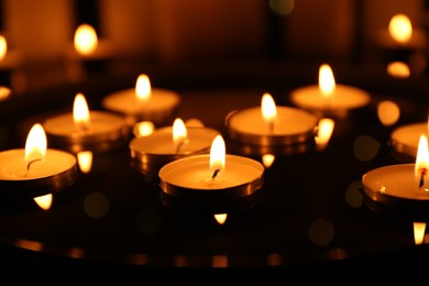 Photo of Many burning candles on dark surface, closeup