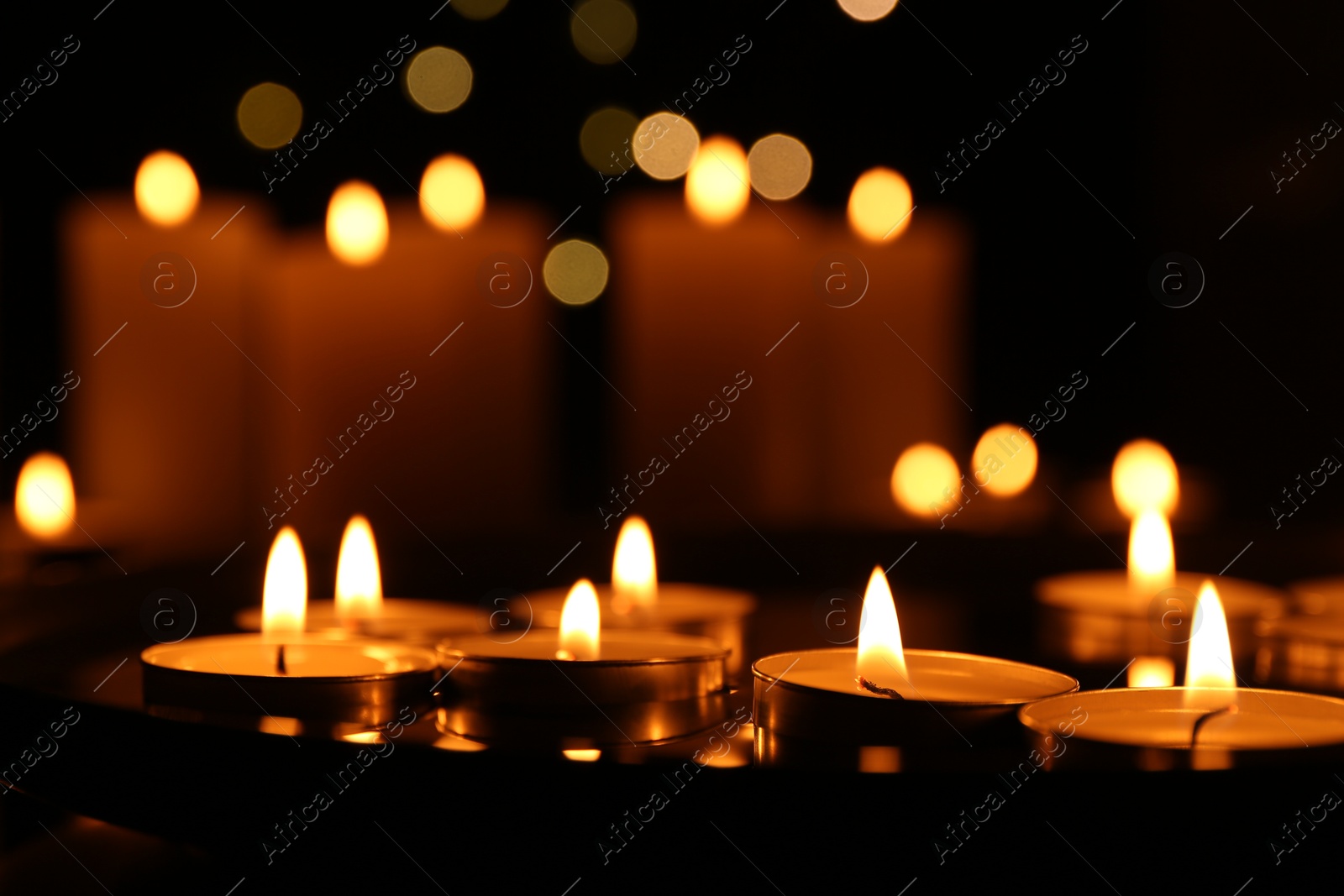 Photo of Many burning candles on dark surface, closeup. Bokeh effect