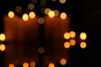 Photo of Blurred view of burning candles in darkness, bokeh effect