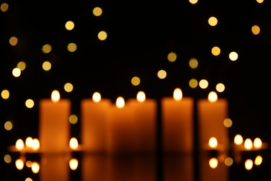 Photo of Blurred view of burning candles in darkness, bokeh effect