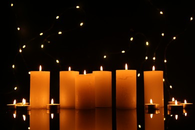 Photo of Many burning candles on mirror surface in darkness