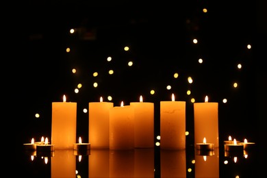 Photo of Many burning candles on mirror surface in darkness