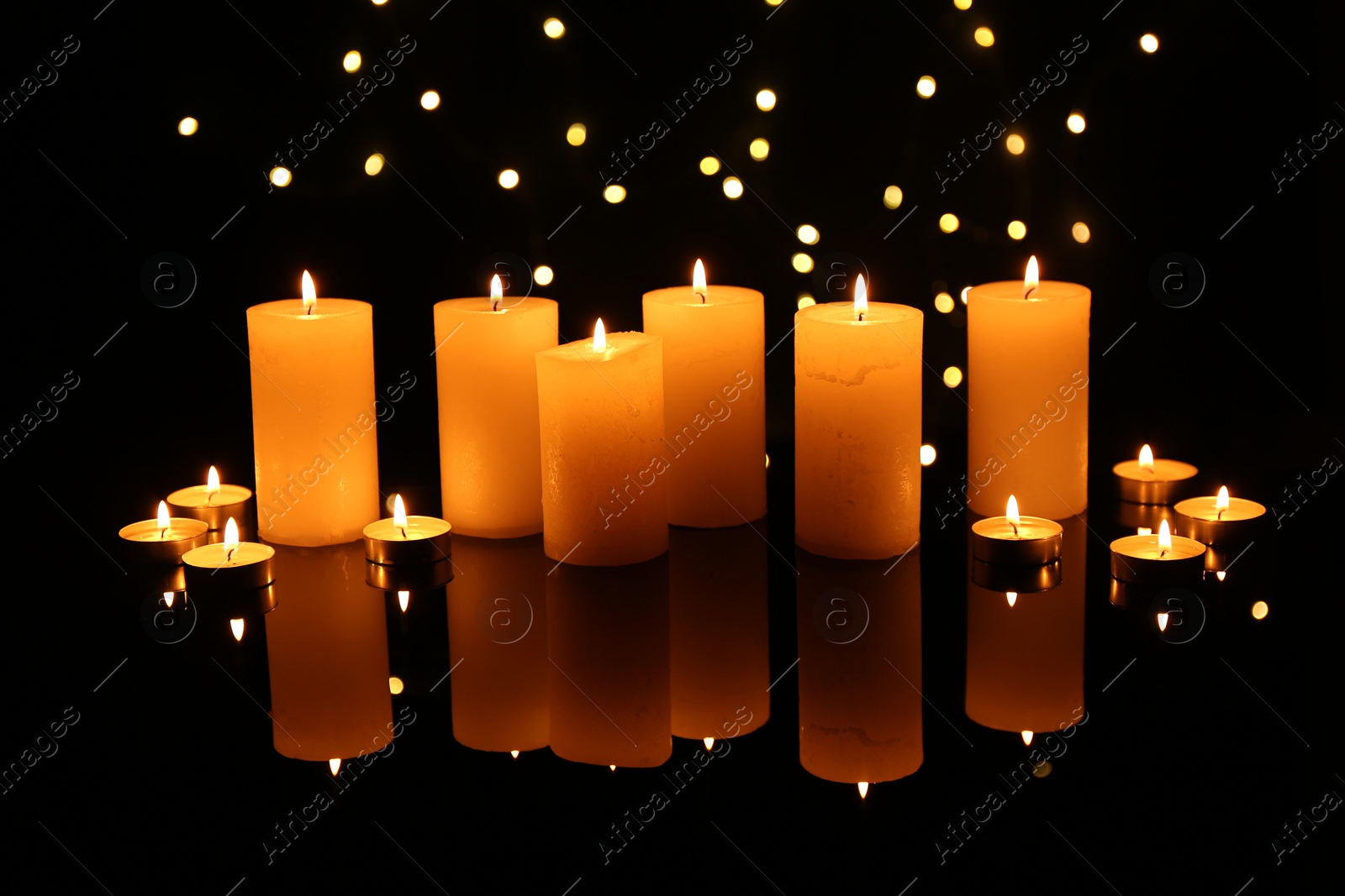 Photo of Many burning candles on mirror surface in darkness