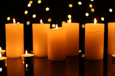 Photo of Many burning candles on mirror surface in darkness