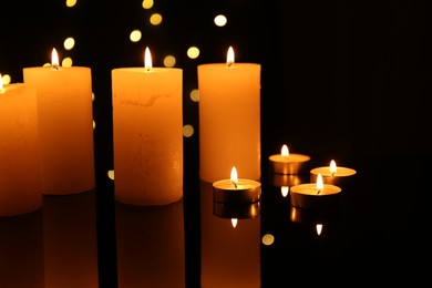 Photo of Many burning candles on mirror surface in darkness