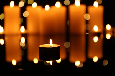 Photo of Burning candles on mirror surface in darkness, closeup. Bokeh effect