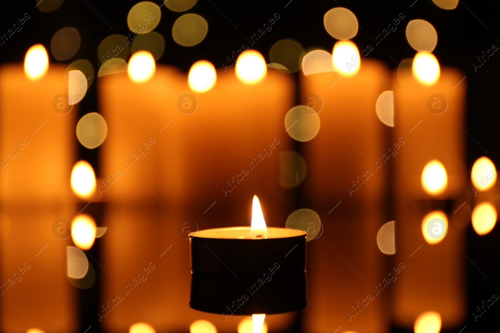 Photo of Burning candles on mirror surface in darkness, closeup. Bokeh effect