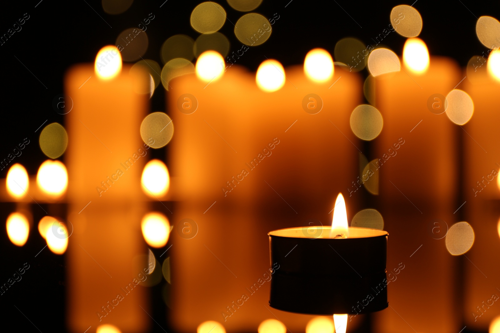 Photo of Burning candles on mirror surface in darkness, closeup. Bokeh effect