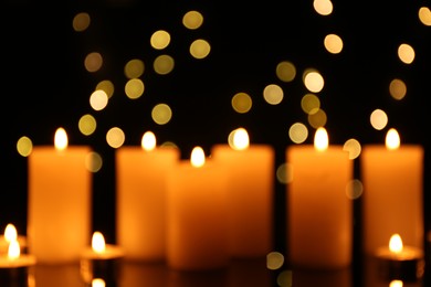 Photo of Blurred view of burning candles in darkness, bokeh effect