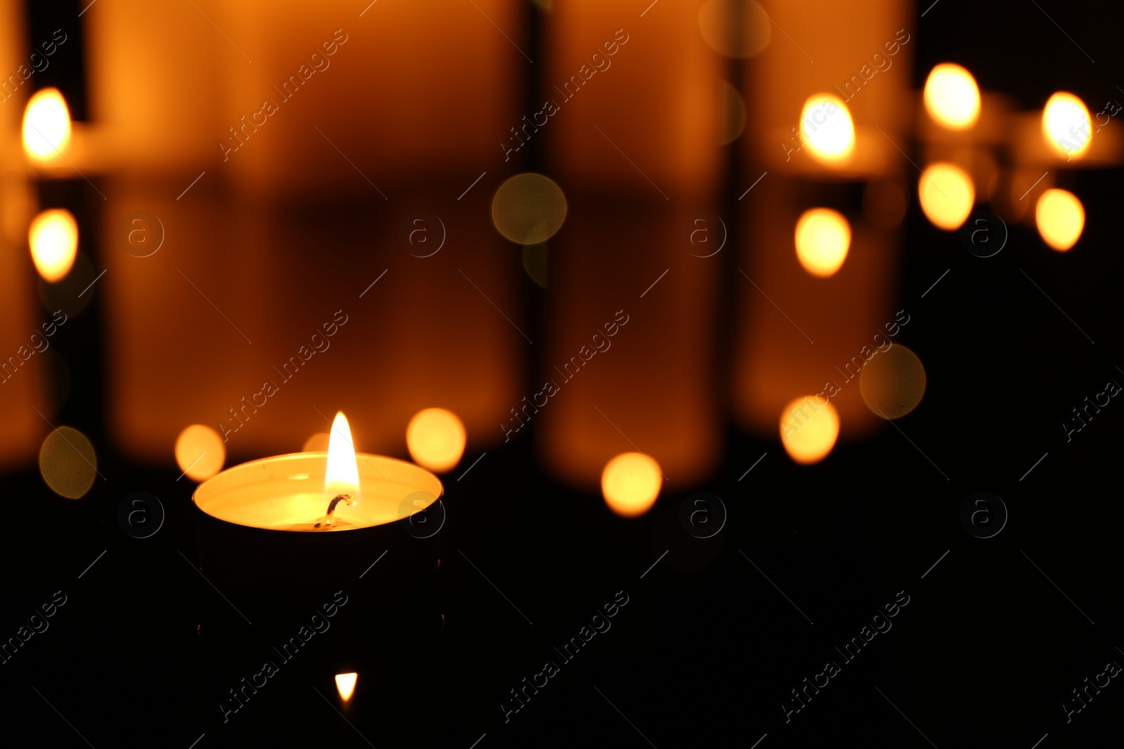 Photo of Burning candles on mirror surface in darkness, closeup. Space for text