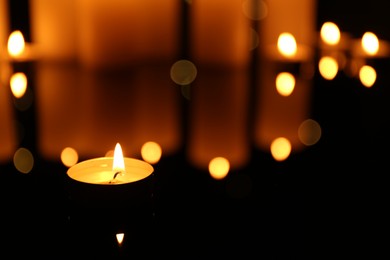 Photo of Burning candles on mirror surface in darkness, closeup. Space for text