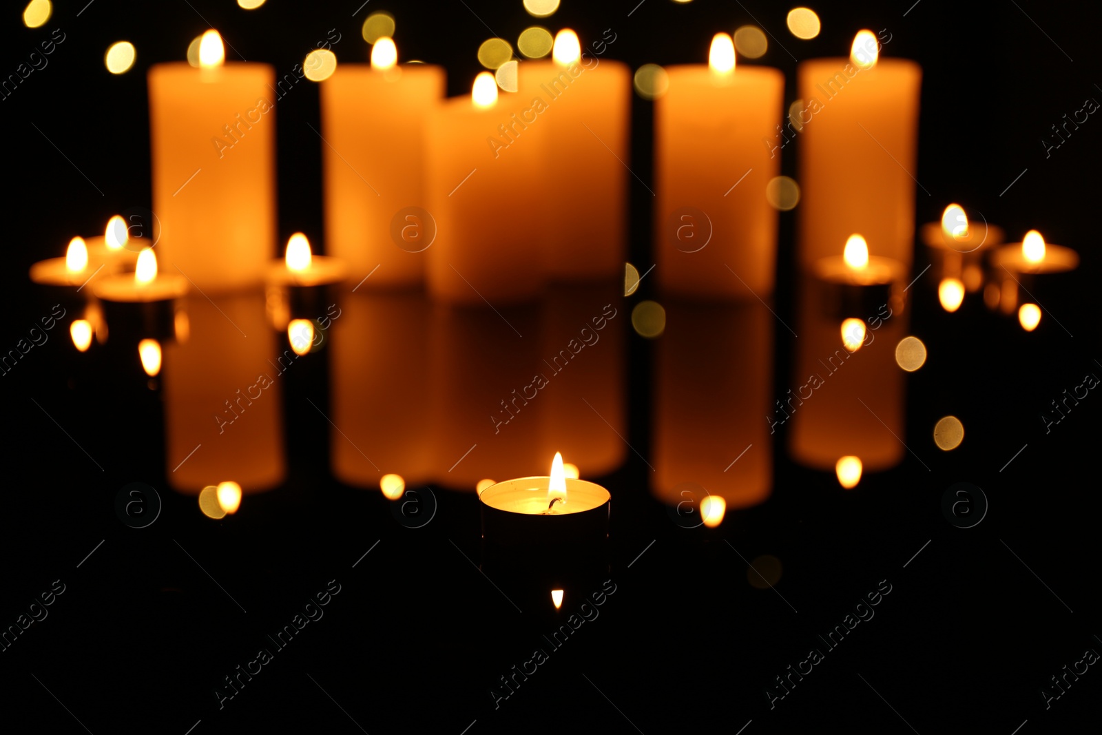 Photo of Burning candles on mirror surface in darkness. Bokeh effect