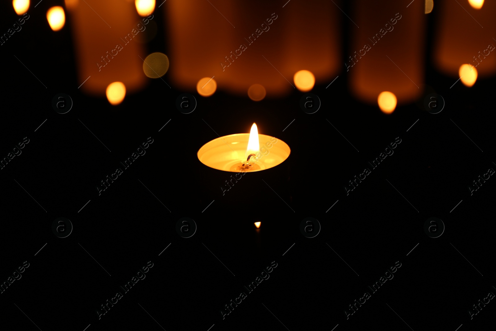 Photo of Burning candle on dark surface, closeup. Bokeh effect