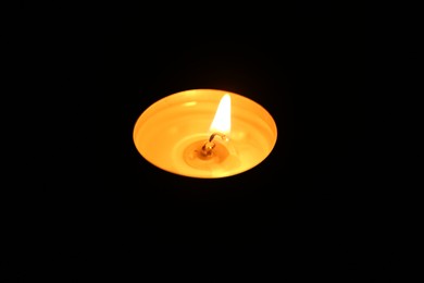 Photo of One burning candle in darkness, closeup view