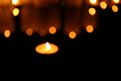 Photo of Blurred view of burning candles in darkness, bokeh effect