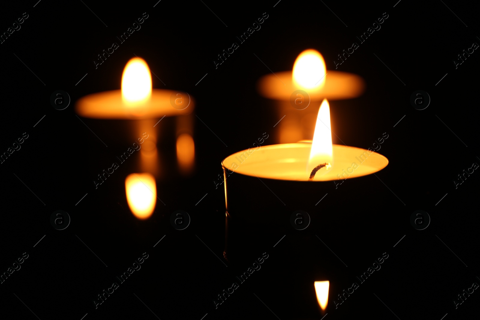 Photo of Burning candles on surface in darkness, closeup