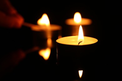 Photo of Burning candles on surface in darkness, closeup