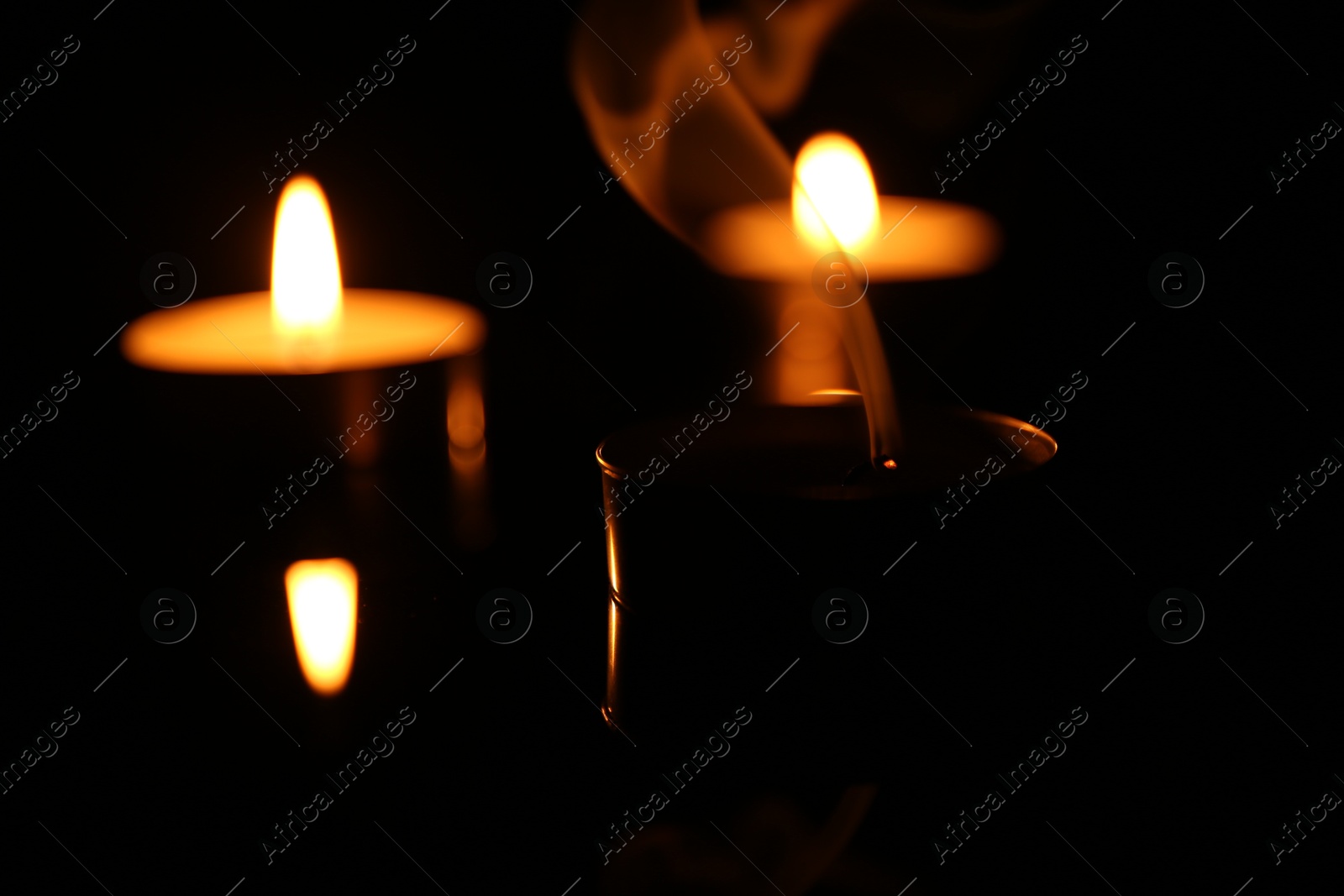 Photo of Burning and smoldering candles on surface in darkness, closeup