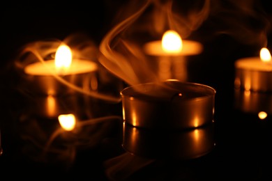 Photo of Burning and smoldering candles on surface in darkness, closeup