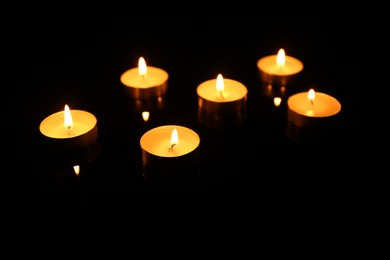 Photo of Many burning candles in darkness, closeup view