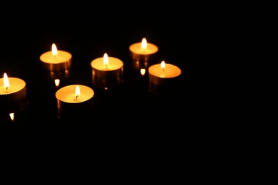 Photo of Many burning candles in darkness, space for text