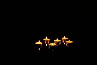 Photo of Many burning candles in darkness, space for text