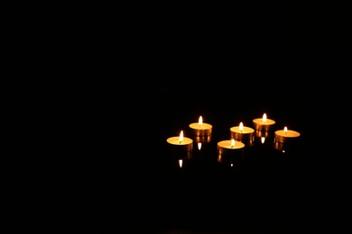 Photo of Many burning candles in darkness, space for text