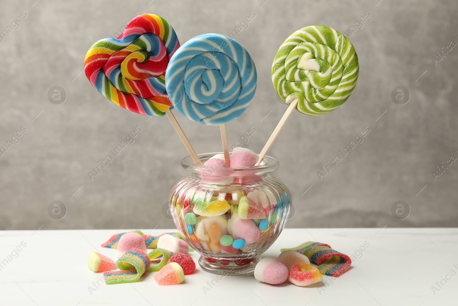 Photo of Different tasty candies on white table against grey background