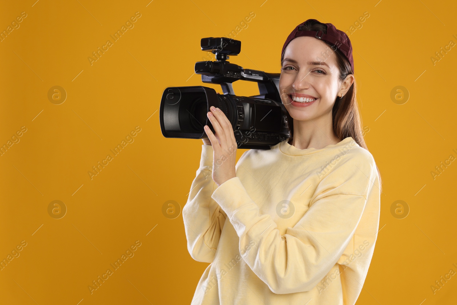 Photo of Happy woman with professional video camera on orange background, space for text