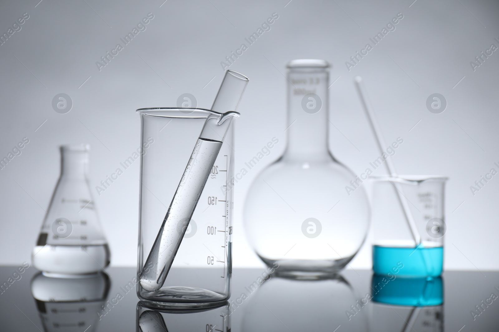 Photo of Laboratory glassware with liquid on mirror surface against light background