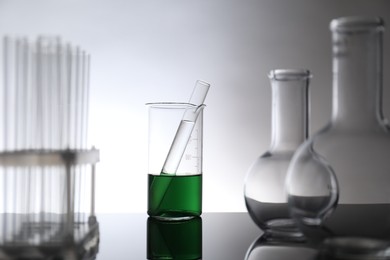 Photo of Laboratory glassware with liquid on mirror surface against light background