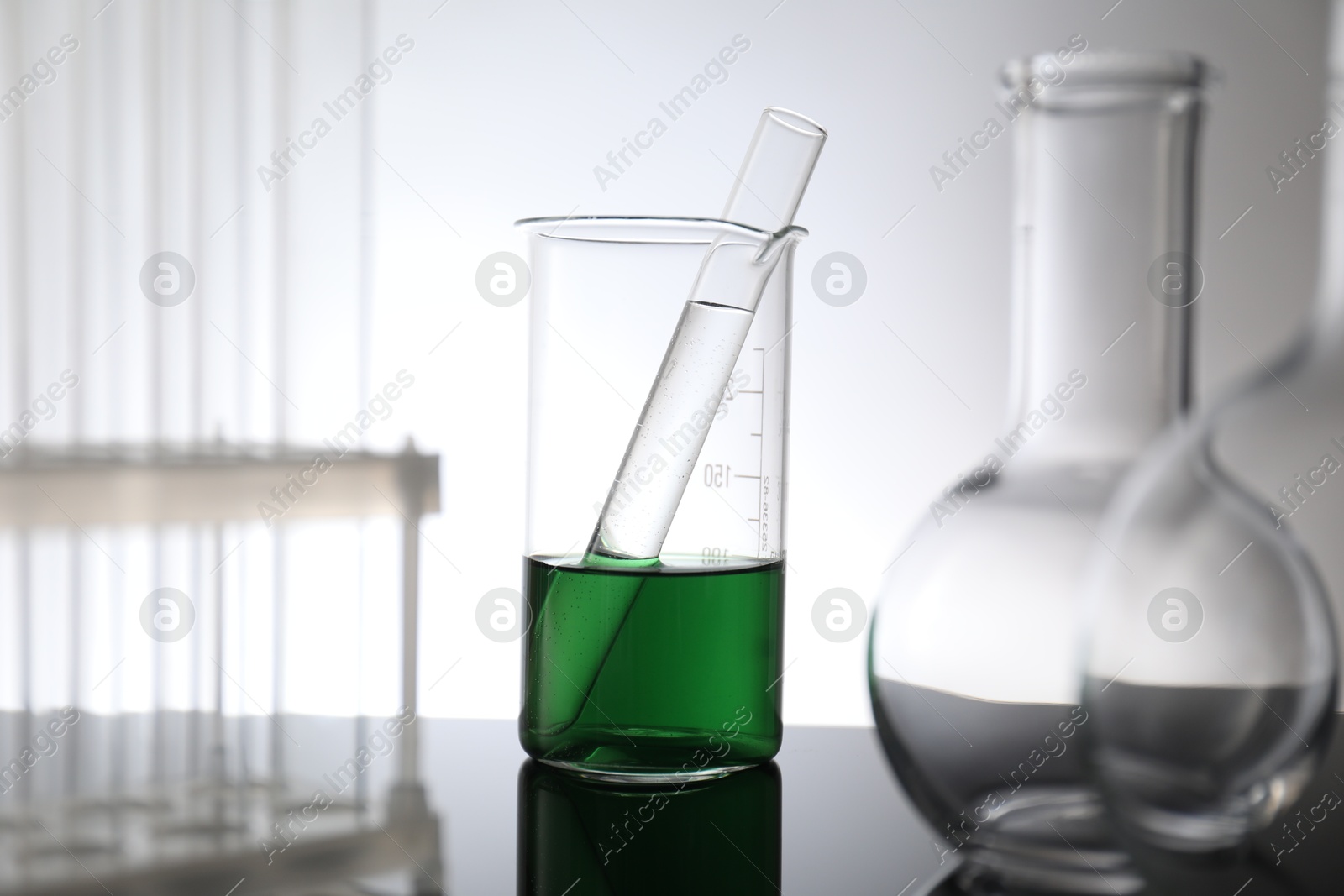 Photo of Laboratory glassware with liquid on mirror surface against light background