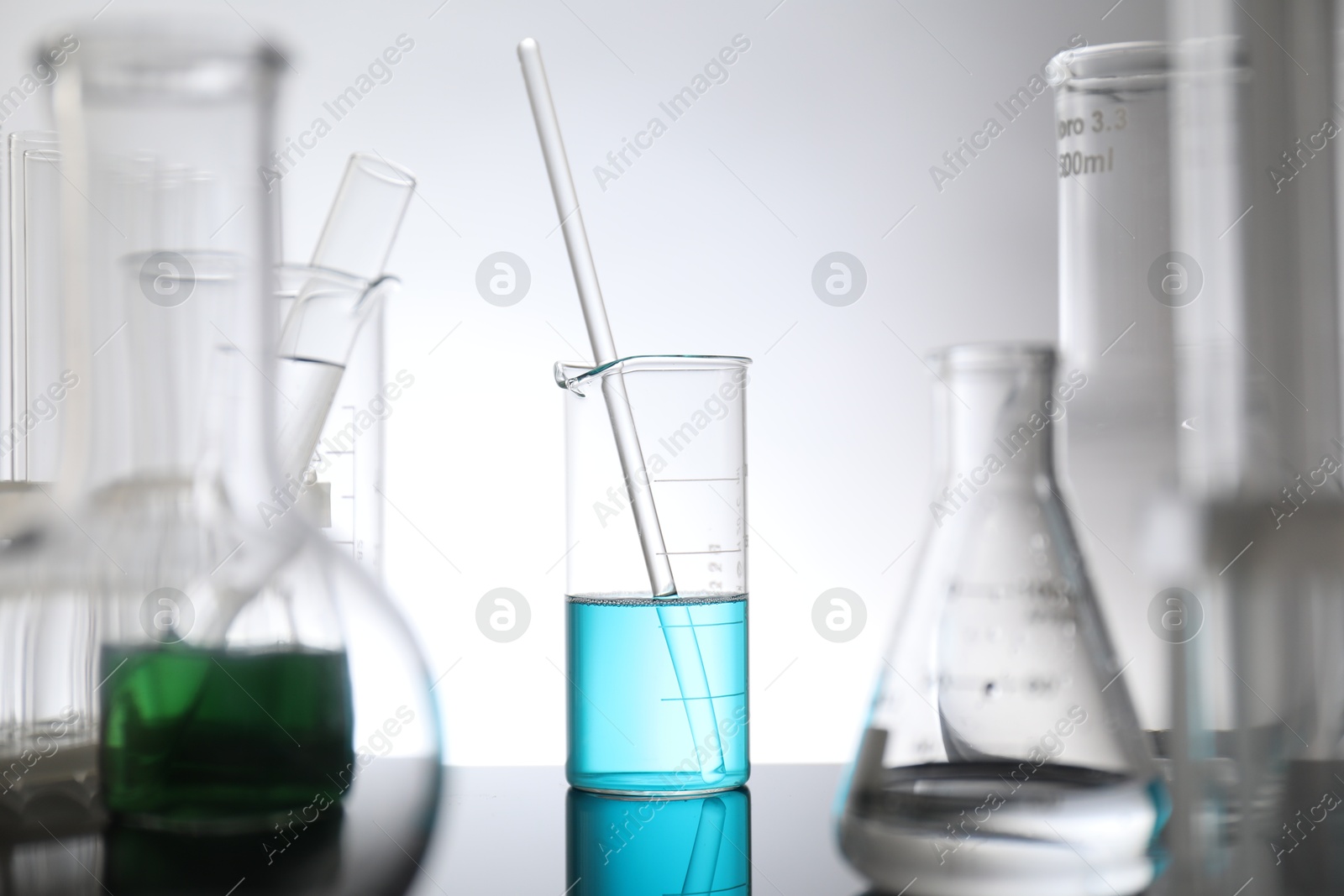 Photo of Laboratory glassware with liquid on mirror surface against light background