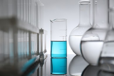 Photo of Laboratory glassware with liquid on mirror surface against light background