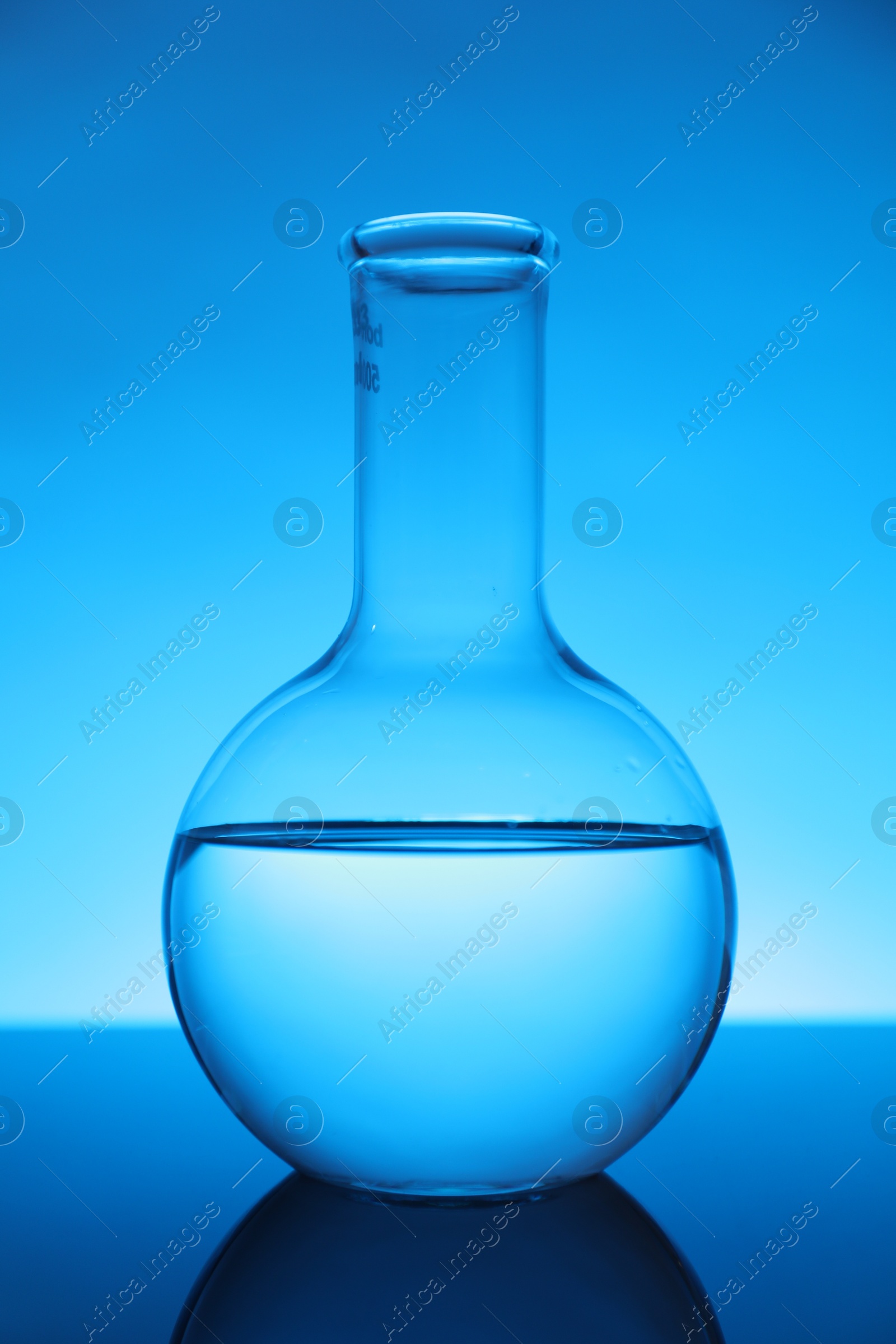 Photo of Flask with liquid on mirror surface against light blue background. Laboratory equipment