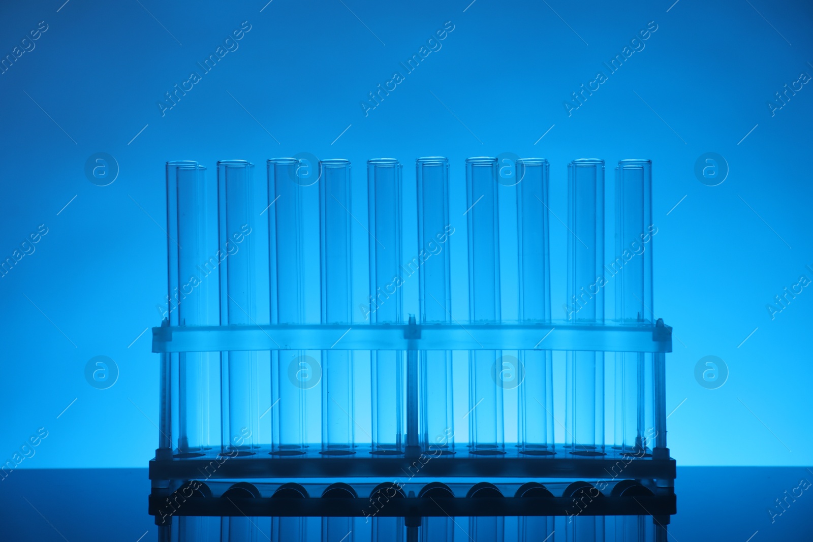 Photo of Test tubes on mirror surface against light blue background. Laboratory glassware