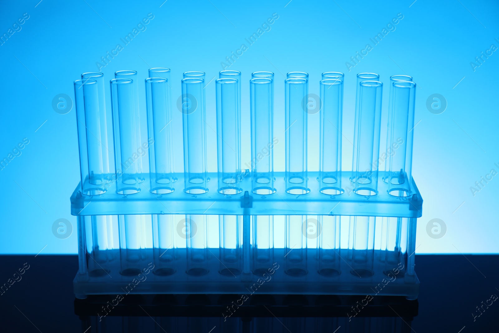 Photo of Test tubes on mirror surface against light blue background. Laboratory glassware