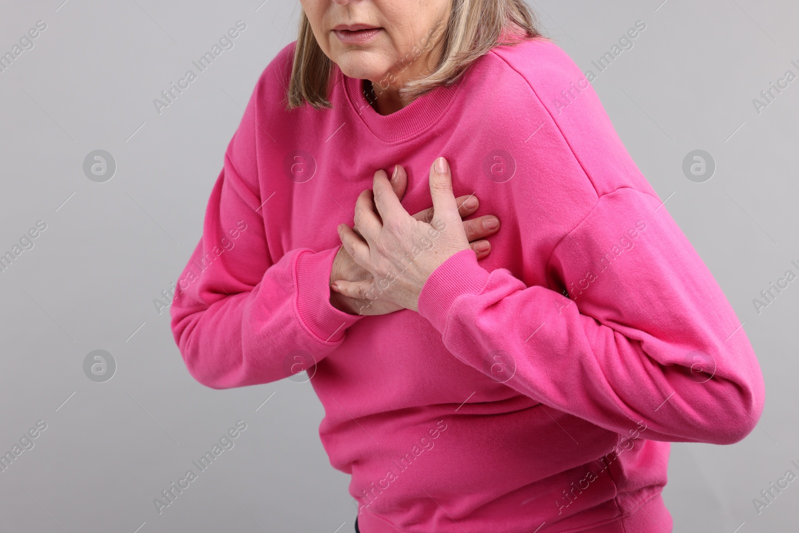 Photo of Heart attack. Senior woman suffering from pain in chest on light grey background, closeup