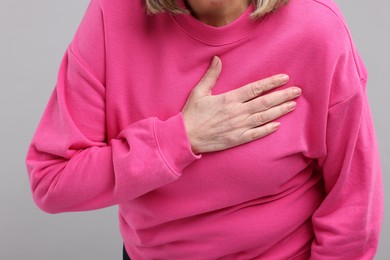 Photo of Heart attack. Senior woman suffering from pain in chest on light grey background, closeup