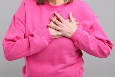 Photo of Heart attack. Senior woman suffering from pain in chest on light grey background, closeup