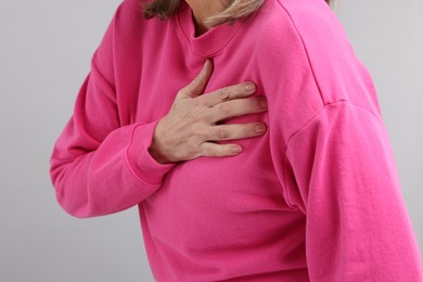 Photo of Heart attack. Senior woman suffering from pain in chest on light grey background, closeup