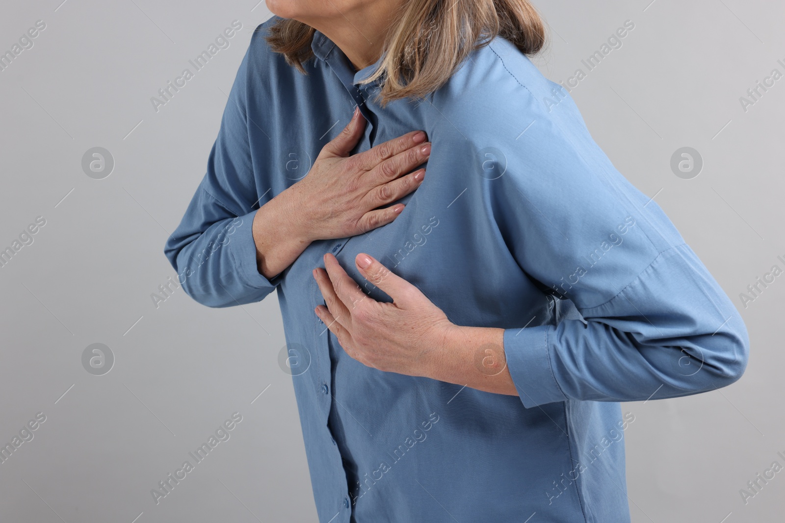 Photo of Heart attack. Senior woman suffering from pain in chest on light grey background, closeup