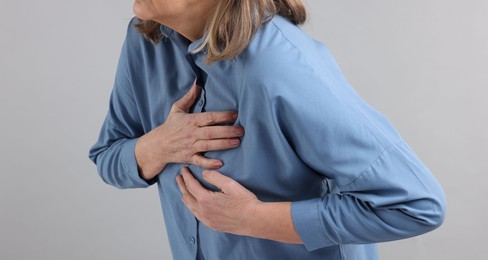 Photo of Heart attack. Senior woman suffering from pain in chest on light grey background, closeup