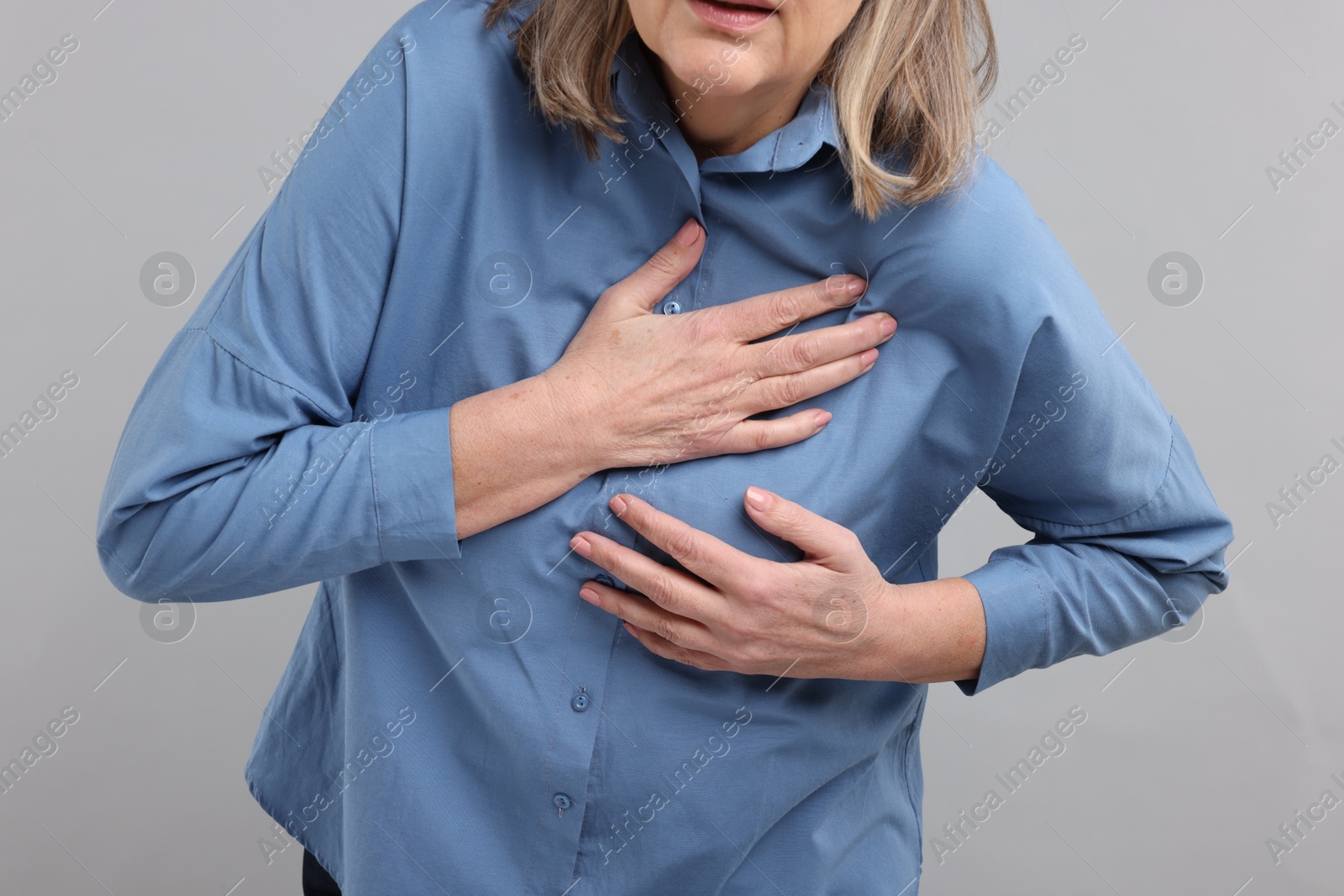 Photo of Heart attack. Senior woman suffering from pain in chest on light grey background, closeup