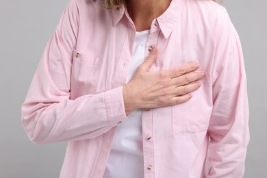 Heart attack. Senior woman suffering from pain in chest on light grey background, closeup