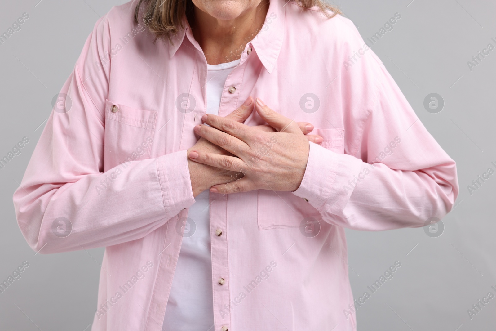 Photo of Heart attack. Senior woman suffering from pain in chest on light grey background, closeup