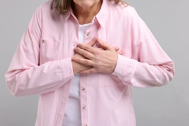 Heart attack. Senior woman suffering from pain in chest on light grey background, closeup