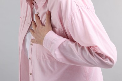 Heart attack. Senior woman suffering from pain in chest on light grey background, closeup